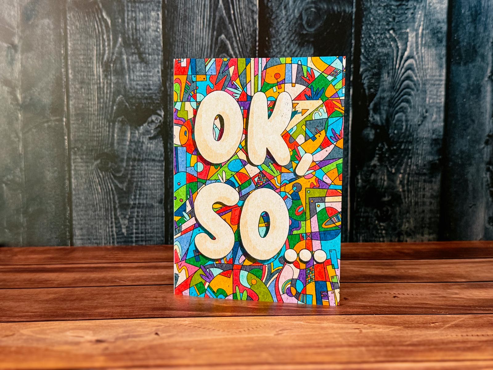 Colorful book with 'OK, SO...' text on a wooden surface and dark wooden panel background