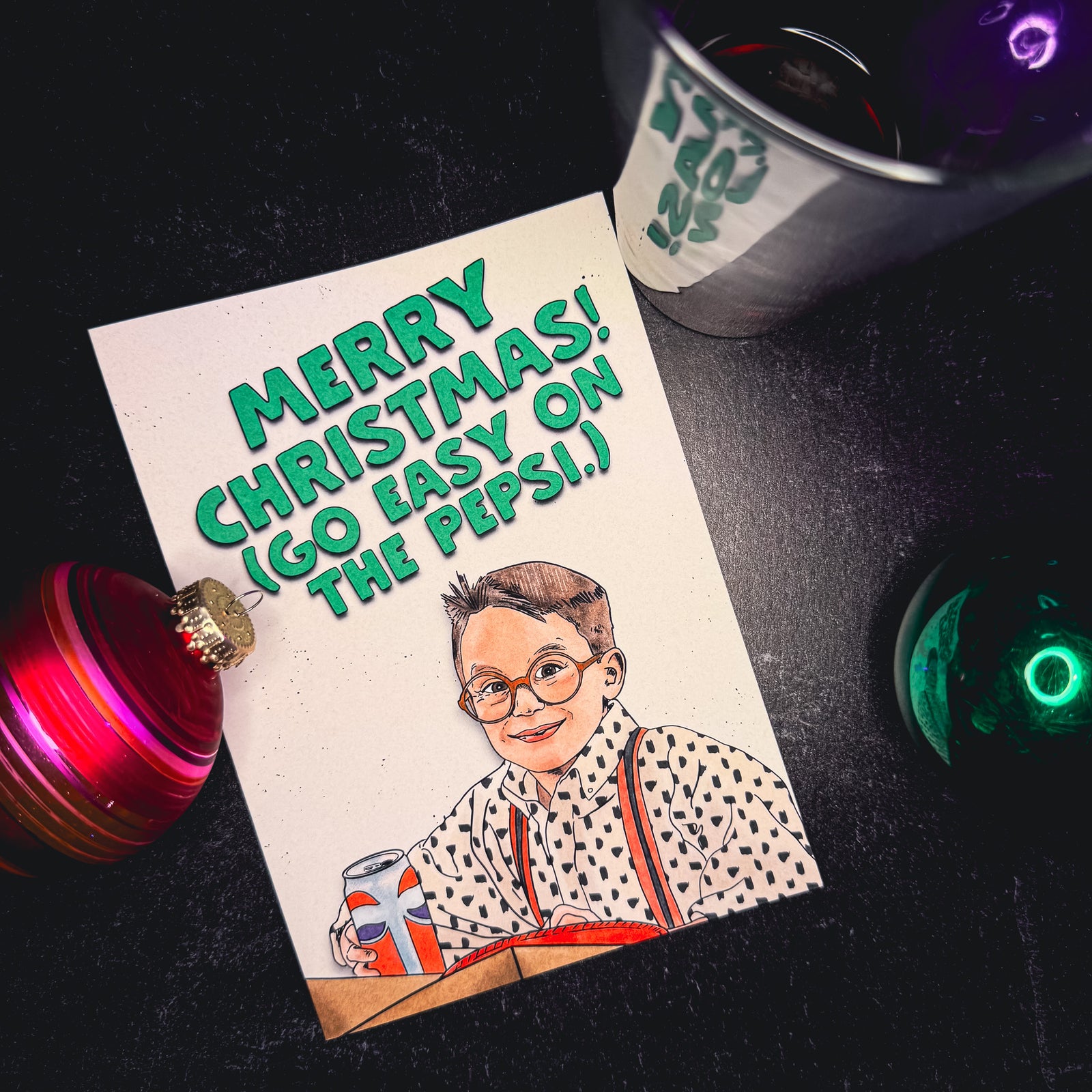 Christmas card with a vintage-style illustration of a boy with a can of soda, surrounded by festive decorations on a dark surface.
